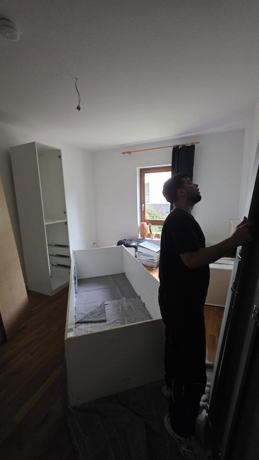 Mitarbeiter von Mars Umzüge steht im Schlafzimmer neben einem weißen Möbelkorpus, der mit einer Möbeldecke ausgelegt ist, im Hintergrund ein offenes Schrankregal